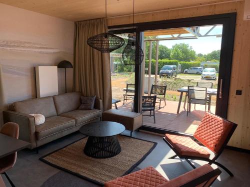 een woonkamer met een bank en stoelen en een patio bij Luxe vakantielodge in Callantsoog aan zee in Callantsoog