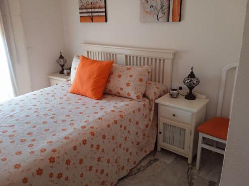 1 dormitorio con 1 cama con almohada naranja y mesita de noche en Apartamento La Caracola en Chiclana de la Frontera