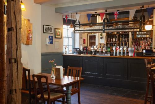 a bar in a restaurant with a wooden table at Cock Hotel by Greene King Inns in Stony Stratford