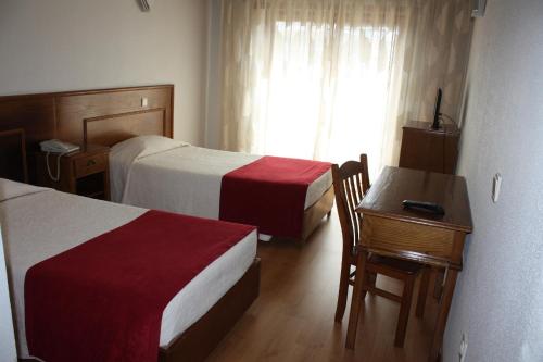 a hotel room with two beds and a desk and a window at Hotel Classis in Bragança