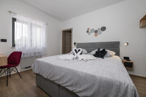 a white bedroom with a large bed with a red chair at Villa Alison Deluxe Junior with private spa and heated swimming pool in Nedeščina