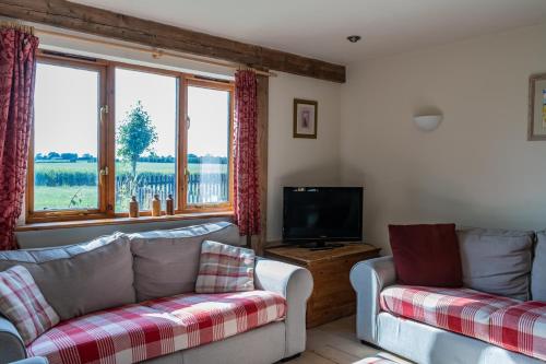 a living room with two couches and a tv at Cart Lodge - Holly Tree Barns in Halesworth