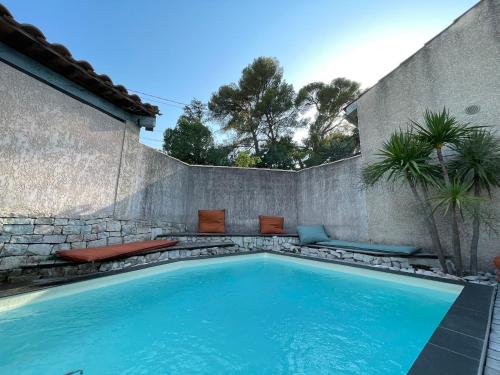 una piscina con bancos junto a una pared en Jolie villa à quelques pas du centre-ville., en Nimes