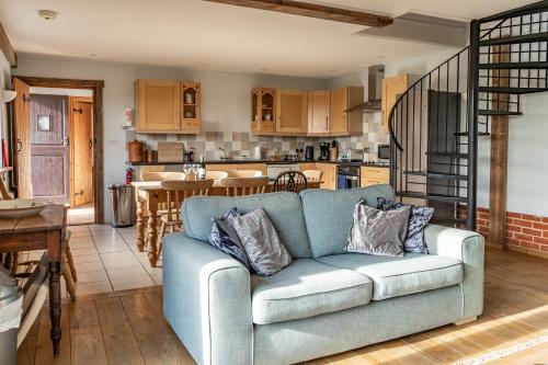 a living room with a blue couch and a kitchen at The Dairy - Holly Tree Barns in Halesworth
