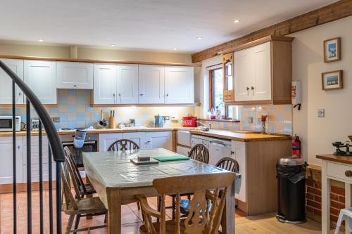 a kitchen with white cabinets and a table and chairs at The Stables - Holly Tree Barns in Halesworth