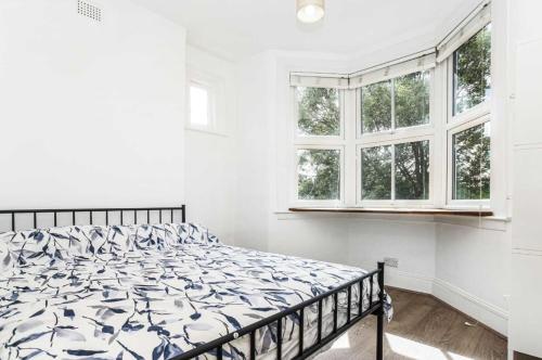 a bed in a white bedroom with windows at Bright and Stylish 2 Bedroom First Floor Flat in London