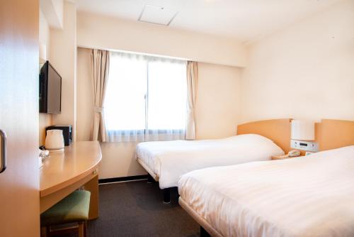 a hotel room with two beds and a desk and a window at le Lac Hotel Yokkaichi in Yokkaichi