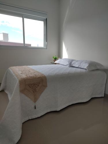 a bedroom with a white bed with a window at Praia de Palmas - Lindo Apartamento in Governador Celso Ramos