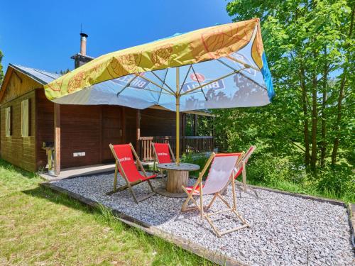 a group of chairs and an umbrella in front of a cabin at Holiday Home Lesní plovárna B1 by Interhome in Mladé Buky