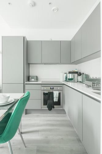 a white kitchen with a table and a green chair at Elegant apartment in Milton Keynes