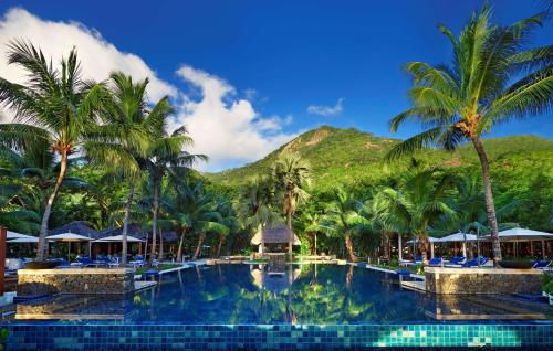 a pool with palm trees and a mountain in the background at Hilton Seychelles Labriz Resort & Spa in Silhouette Island