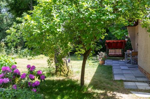 einen Garten mit einem Baum, einer Bank und Blumen in der Unterkunft Ferienhaus Krohse in Potsdam
