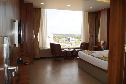 a hotel room with a bed and chairs and a window at Hotel Varun Mansion Hassan in Hassan
