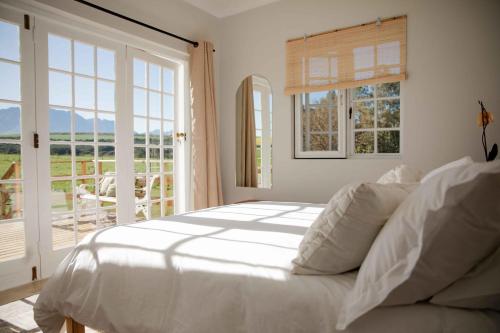 ein weißes Schlafzimmer mit einem Bett und einem Balkon in der Unterkunft Melkhout River Cottage in Bonnievale