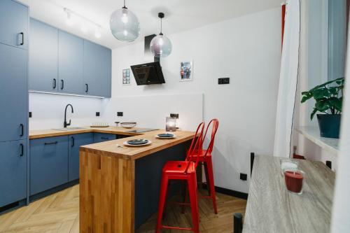a kitchen with blue cabinets and a wooden island with two red stools at Apartament Lwowska in Lublin