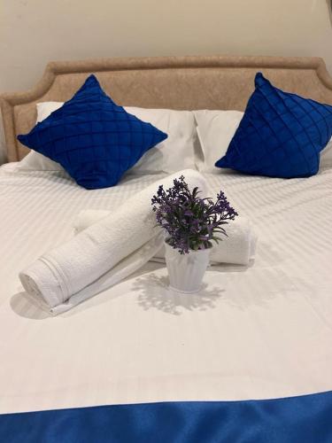 a white bed with blue pillows and a vase of flowers at Level 12 Riverbank suites 2BR RiverView in Kuching