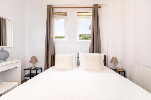 um quarto com uma cama branca e 2 janelas em Ktima Petrina Volia- Maisonette Phos em Andros