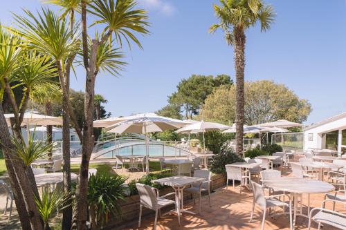 un patio con mesas, sillas y palmeras en Fleur de Sel en Noirmoutier-en-l'lle