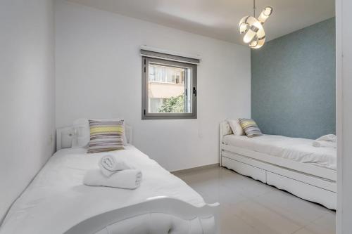 a white bedroom with two beds and a window at Trust Inn garden in the city in Tel Aviv