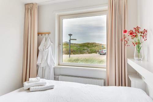 a bedroom with a window and a white bed with towels at Zeezicht Villa Strand direct bij zee in Bergen aan Zee