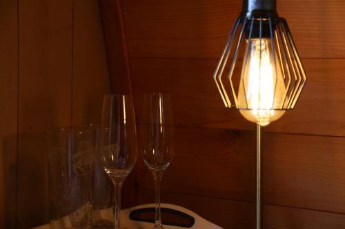 three wine glasses sitting on a table with a lamp at Knapp Farm Glamping Puki Pod in Corscombe