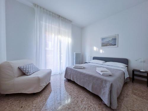 een witte slaapkamer met een bed en een stoel bij La Roscia House in Porto San Giorgio