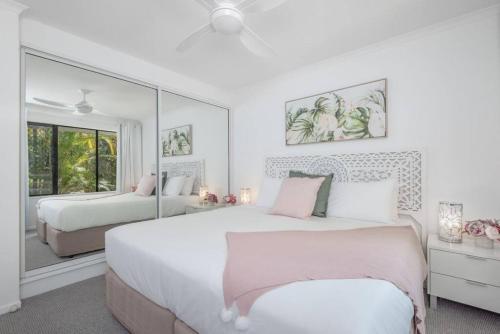 a white bedroom with two beds and a mirror at Tranquil Noosa retreat minutes from the river 40IP in Noosaville