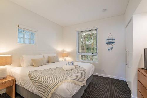 a white bedroom with a bed and a window at Poolside luxury on Hastings St 212 in Noosa Heads