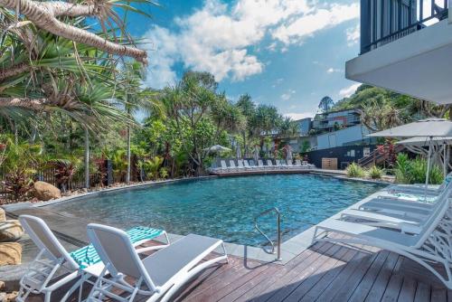 a swimming pool with chaise lounge chairs next to a house at Tranquil treetop retreat minutes from the beach 7405 in Noosa Heads