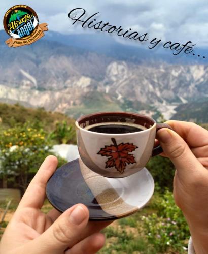 a person holding a cup of coffee in front of a mountain at HOTEL CAMPESTRE ABRAZO DEL ANGEL in Aratoca