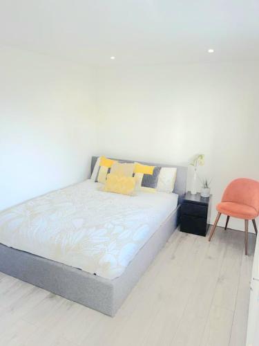 a bed in a white room with a orange chair at Modern 2 Bedroom Flat With Garden LONDON in Northolt