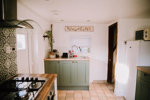 una cocina con armarios verdes y fregadero en Pebbles Cottage, en Caister-on-Sea