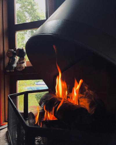 a fire burns in a fireplace in front of a window at Chalé Cores da Mata in Brumadinho