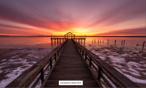 a wooden bridge leading into the water with a sunset at Comfy Retreat Balcony Views Amenities in Woodbridge