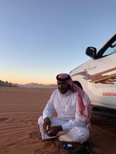a man sitting in the desert next to a car at Desert's Soul Wadi Rum in Disah