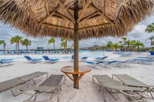 a table and chairs under a straw umbrella on the beach at Modern Oasis! 3BR Townhouse in a Lagoon Community in Wesley Chapel