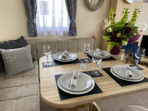 a dining room table with plates and wine glasses at Comfy Cosy Caravan_Romney Sands in Littlestone-on-Sea