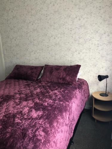 a bedroom with a purple bed and a lamp on a table at Nights on Broadway - THE HOUSE in Matamata