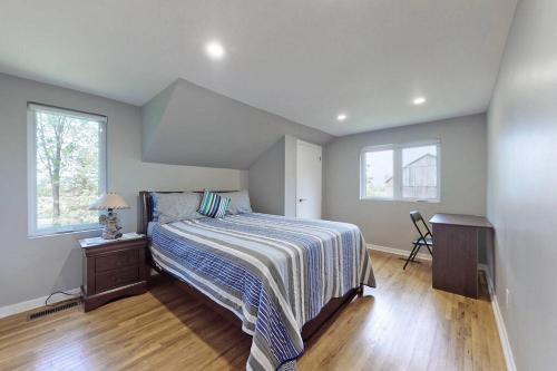 a bedroom with a bed with a striped blanket and two windows at Hidden Farm Escape in the Heart of Kawarthas in Beaverton