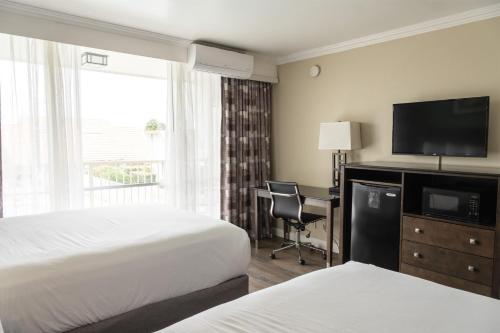 a hotel room with two beds and a desk with a television at Travelodge by Wyndham Monterey Bay in Monterey