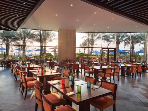 a restaurant with wooden tables and chairs and windows at Fairmont Ajman in Ajman 
