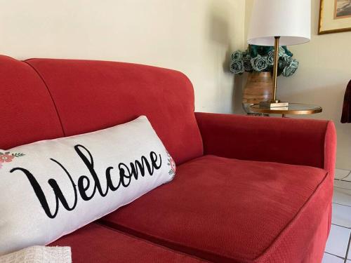 a red couch with a pillow with the word welcome at Comfy and Quiet APT 5 min Walk to Historic Downtown in Saint Augustine