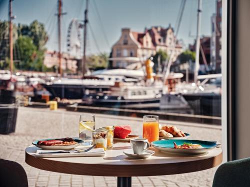 a table with plates of food and drinks and a view of a harbor at Holiday Inn Gdansk - City Centre by IHG in Gdańsk