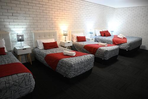 a room with three beds with red pillows at Cameo Inn Motel in West Wyalong