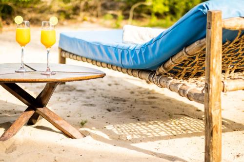 two wine glasses on a table next to a hammock at Simply Saadani Camp, A Tent with a View Safaris in Mkwaja