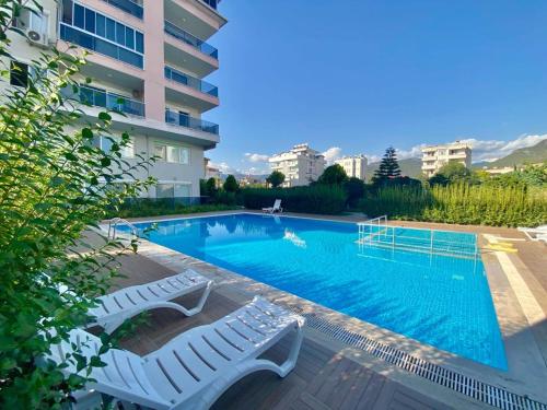 a swimming pool with two white chairs next to a building at Kestel Квартира возле моря in Çamyolu