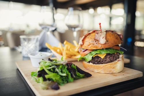 a hamburger and french fries on a cutting board with a salad at Van der Valk Hotel Saint-Aygulf in Saint-Aygulf