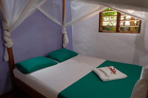 białe łóżko z zielonymi poduszkami i oknem w obiekcie Villa Ilo Komba w mieście Nosy Komba