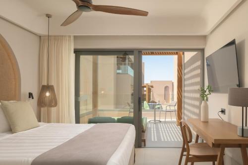 a bedroom with a bed and a desk and a balcony at Paralos Venus Suites Adults Only in Hersonissos