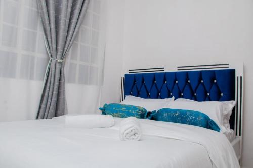 Cama blanca con cabecero azul y almohadas en Cool 1 B/Room Thika Road en Nairobi